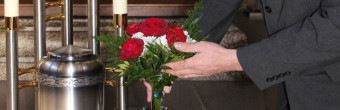 Hand mit Blumenstrauß bei der Urne